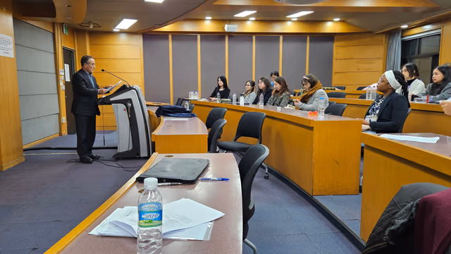 A speaker reads the founding address from the lectern while members listen from the tiered desks