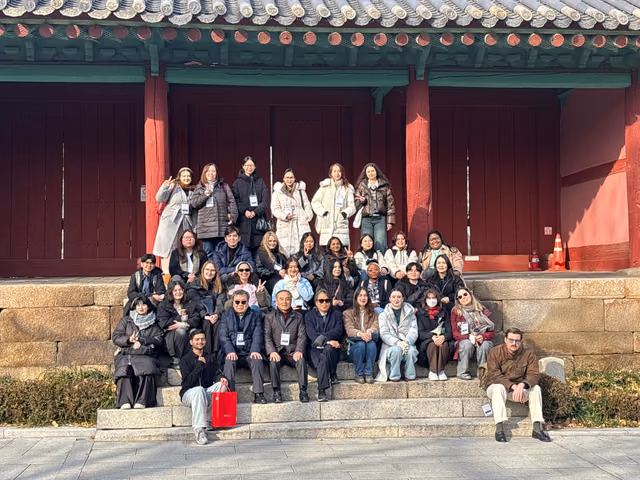 About thirty-five members and guests seated and standing on the stone steps of a traditional hall at Myeongnyun Campus